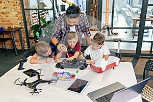 Male electronic engineer with european school children working in smart school lab and testing model of radio controlled