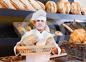 Male employee offering fresh baguettes and buns in bakery
