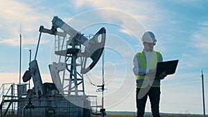 Male energetics worker is standing with a laptop next to a petrol derrick