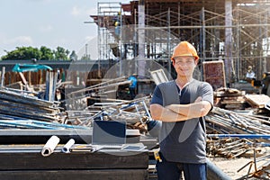 Male Engineer with arms crossed standing at a construction site looking happy