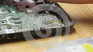 Male engineer computer repair works with disassembled laptop. One can see the computer`s motherboard. Wooden table top