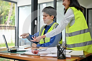 A male engineer is discussing a building blueprint on a desktop with his female colleague