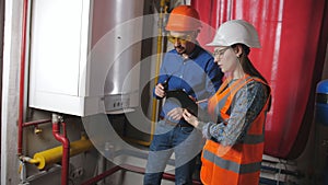 Male engineer and a female checker check operability of equipment in the boiler room. The woman enters the data into