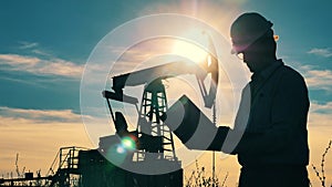 Male engineer and a functioning pumpjack in sunlight. Oil and gas industry concept.