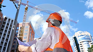 Male engineer holding construction drawings outdoor while standing in construction site. Business, building, industry