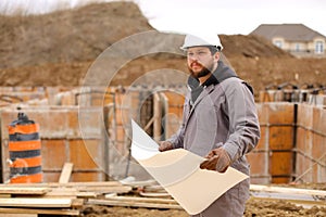 Male engineer holding drawing plan of hause at construction site.