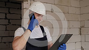 A male engineer holds a paper folder with information and talks on the phone.