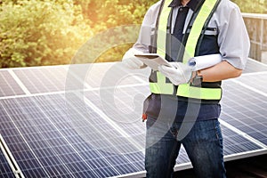 A male engineer holds a tablet to inspect the solar cell system.