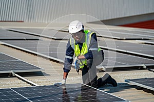 Male engineer maintaining solar cell panels on building rooftop. Technician working outdoor on ecological solar farm construction.