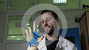 Male engineer scientist experiences a bionic prosthesis of a mechanical arm. He watches the work of the robot`s hands