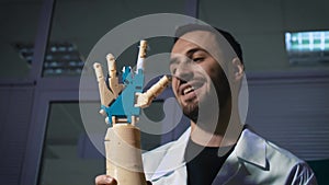 Male engineer scientist experiences a bionic prosthesis of a mechanical arm. He watches the work of the robot`s hands