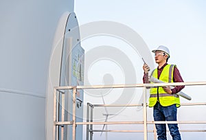 Male engineer using walkie talkie to checking system against wind turbine farm