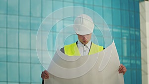 Male Engineer Wearing in Helmet and Safety Jacket, Looking Construction Drawings in his Hand