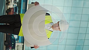 Male Engineer Wearing in Helmet and Safety Jacket, Looking Construction Drawings in his Hand