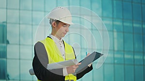 Male Engineer Wearing in Helmet and Safety Jacket, Looking Construction Drawings in his Hand