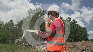 Male engineer wearing helmet and vest talking by phone at construction site