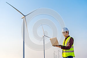 Male engineer working with laptop computer against wind turbine farm