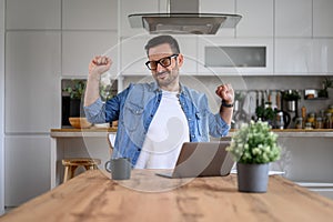 Male entrepreneur with eyes closed stretching arms while working over laptop at desk in home office
