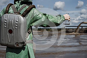 A male environmentalist in a green protective suit and gas mask takes a sample of water in a polluted lake for research