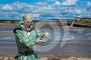 A male environmentalist in a green protective suit and gas mask takes a sample of water in a polluted lake for research