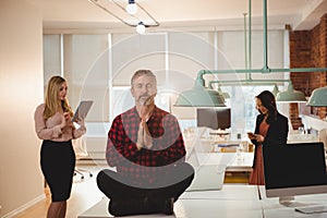 Male executive meditating on table in office