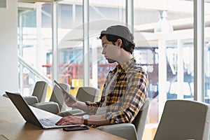 Male executive using digital tablet while working on laptop in the conference room