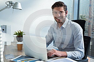 Male executive using laptop while looking at camera