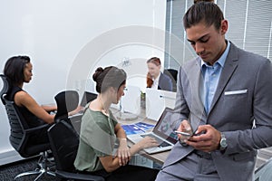 Male executive using mobile phone while colleagues working in background