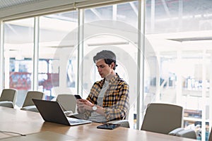 Male executive using mobile phone while working on laptop in the conference room