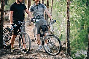 male extreme cyclists in helmets with mountain bikes resting with sport bottles of water