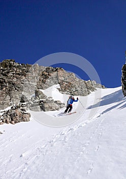 Male extreme skier skiing down a very steep couloir in deep winter in the Swiss Alps near Klosters