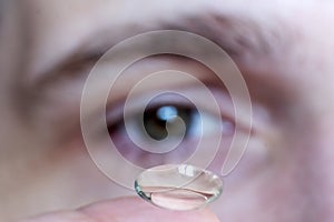 Male eye close-up, contact lens on finger