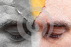 Male eyes are looking down at the forehead sheet. half of the image is colored silver. the arrival of oldness is not avoided