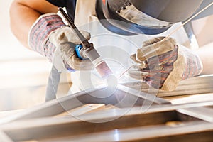 Male in face mask welds with argon-arc welding