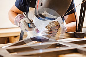 Male in face mask welds with argon-arc welding