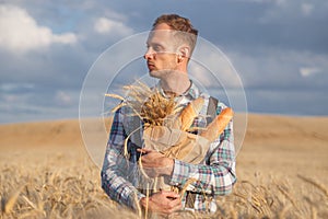 Male farmer or baker with baguettes in rye, wheat field