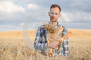 Male farmer or baker with baguettes in rye, wheat field