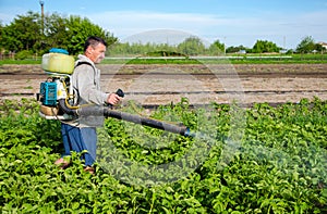 Male farmer with a mist sprayer processes potato bushes with chemicals. Control of use of chemicals. Farming growing vegetables
