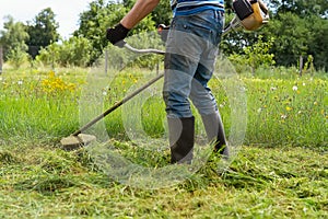 A male farmer mows the tall green grass with a trimmer. Mower-trimmer. A worker mows the grass on the lawn in the garden with a ha