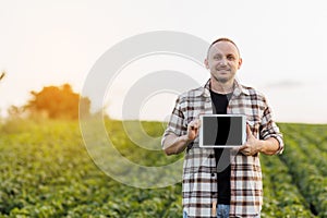 Male farmer shows digital tablet with empty black screen on green soybeans field. Smart farming technology and organic