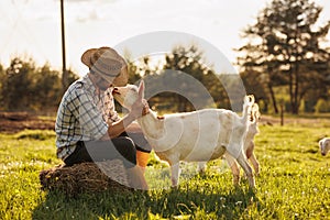 Male farmer taking care of his cute goats. Young rancherman getting pet therapy. Animal husbandry for the industrial