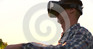 Male farmer in virtual reality glasses in the field at sunset controls the corn irrigation system