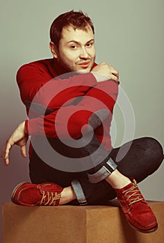 Male fashion concept. Portrait of young man wearing trendy casual purple sweater, blue jeans & red chamois shoes. Guy sitting on