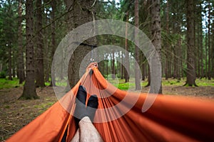 Male feet in black socks resting in the orange hammock hanged in the forest