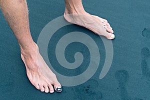 Male feet and footprints on volcanic black sand beach shore