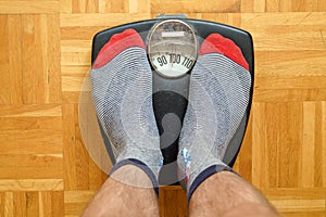 Male feet in funny socks standing on an old scale showing almost 100 kg.