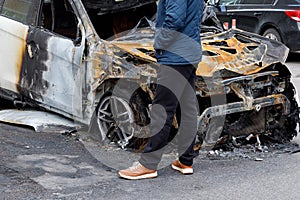 Male feet near the burned-out car. Car with traces of fire, explosion, accident or accident in the background