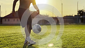 Male feet of professional footballer kicking ball at green field. Legs of young man juggling soccer ball on stadium at