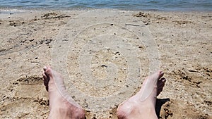 Male feet on sand and pebbles at beach with water