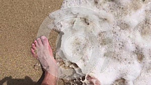 Male feet in shallow water on a beach summer vacation background foreshortening from above
